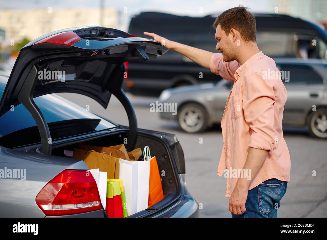 Der Mann legt seine Einkäufe in den Kofferraum auf den Parkplatz Stockfoto