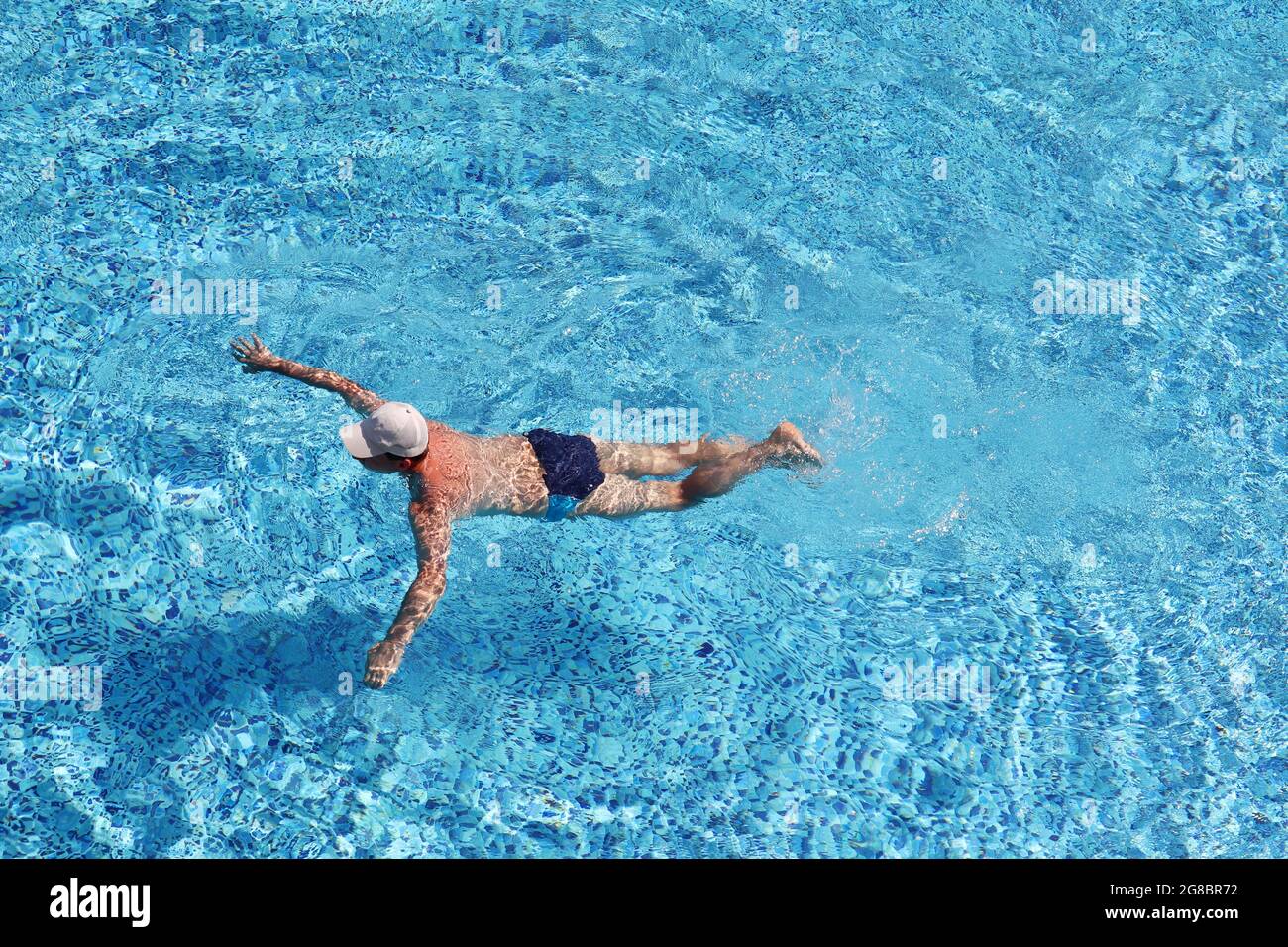 Mann mit Baseballmütze, der im Poolwasser schwimmend ist, Draufsicht. Wassersport, Strandurlaub Stockfoto