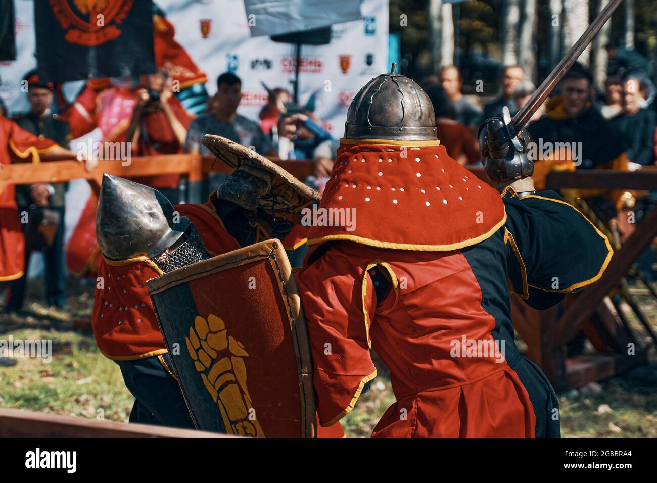 Zwei Ritter kämpfen mit Schwertern. Auf dem Schild des Ritters ist ein Bild eines goldenen Handschuhs zu sehen. Simulation mittelalterlicher Schlachten während des Festivals historischer Vereine. Bischkek, Kirgisistan, 13. Oktober 2019. Stockfoto