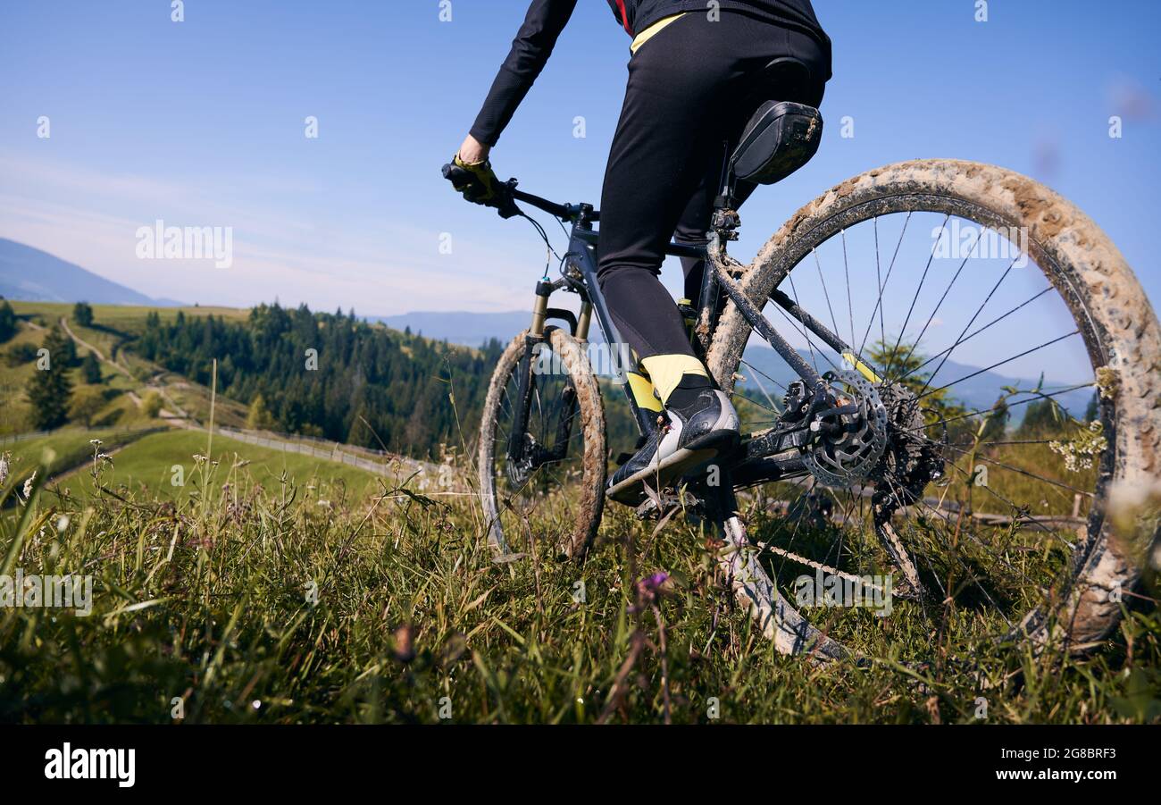Nahaufnahme, niedriger Winkel auf einem Fahrrad mit Radfahrer. Die Beine des Mannes reiten im Sommer auf Gras in den Bergen gegen den blauen Himmel. Konzept des Extremfahrens Stockfoto