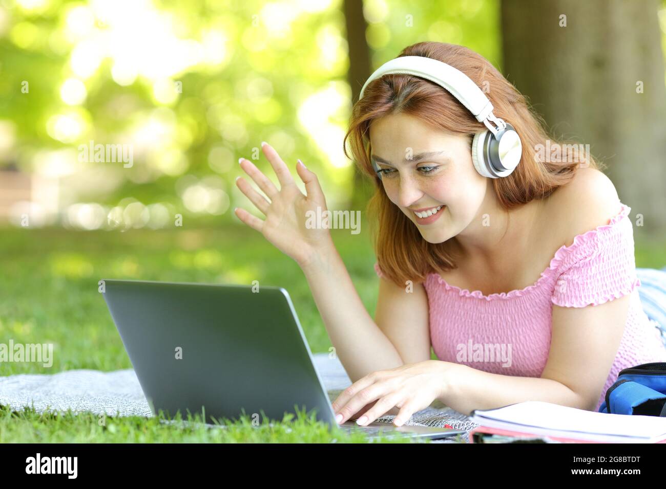 Glückliche Frau, die online mit einem Laptop auf dem Rasen in einem Park Videos macht Stockfoto