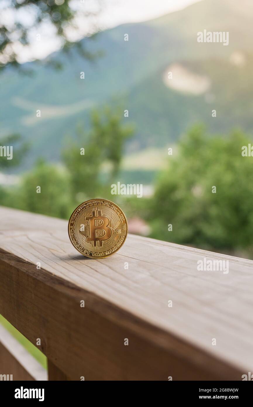 Bitcoin goldene Krypto-Münze auf Holzterrasse mit natürlichem Berg und grünen Bäumen Hintergrund mit Kopierraum. Kryptowährung Mining und Umwelt i Stockfoto