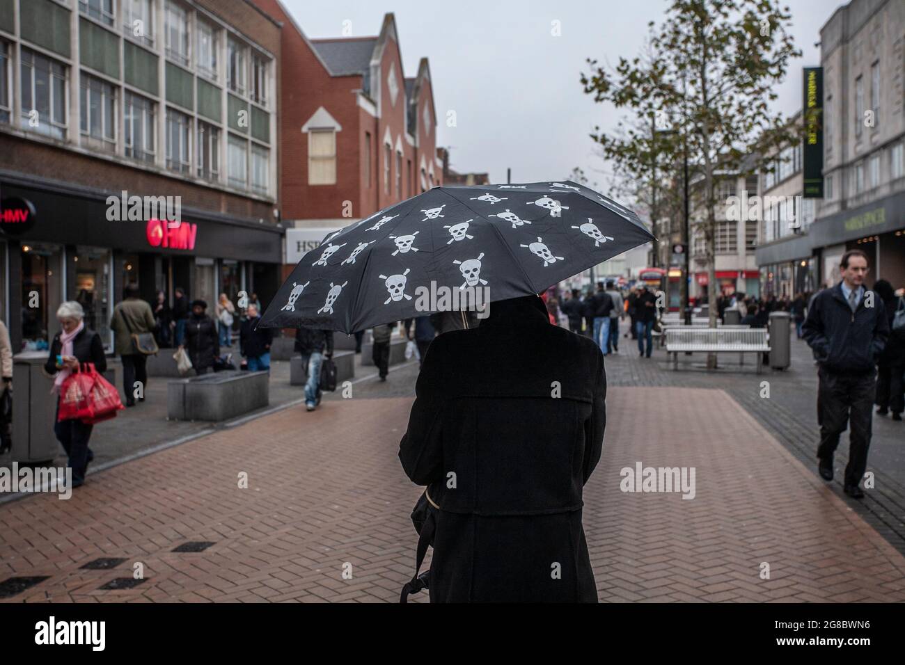 Eine Frau, die die Hauptstraße entlang geht und einen Regenschirm mit „Skull & Crossbones“-Aufdruck hält, während der Einzelhandel mit der Wirtschaft in Croydon, Großbritannien, zu kämpfen hat Stockfoto