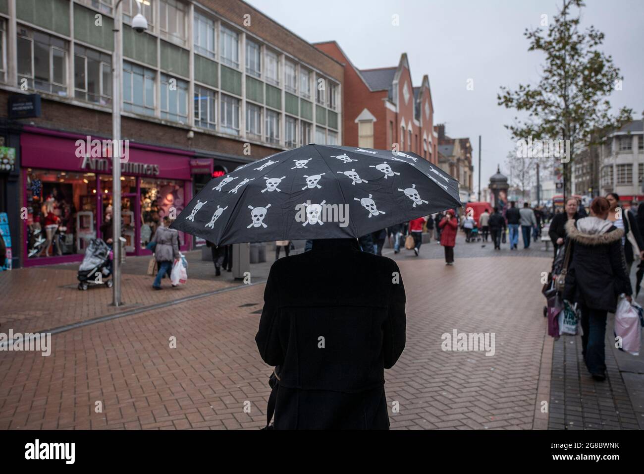Eine Frau, die die Hauptstraße entlang geht und einen Regenschirm mit „Skull & Crossbones“-Aufdruck hält, während der Einzelhandel mit der Wirtschaft in Croydon, Großbritannien, zu kämpfen hat Stockfoto