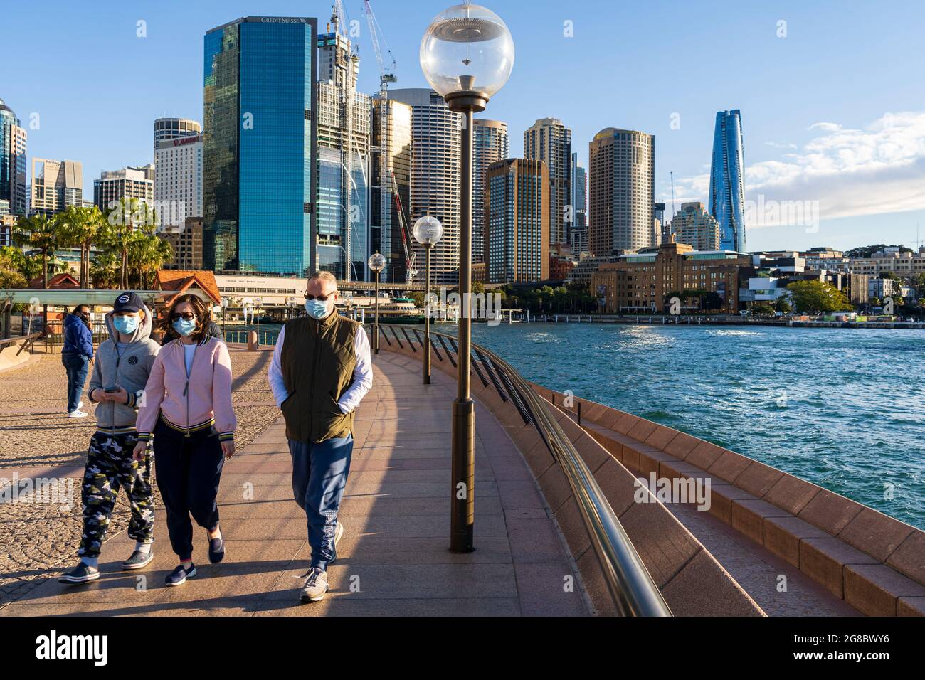 Spaziergänger in Masken trainieren am Circular Quay, Sydney, Australien, während einer Pandemie-Sperre. Blaues Himmel und Skyline im Hintergrund Stockfoto