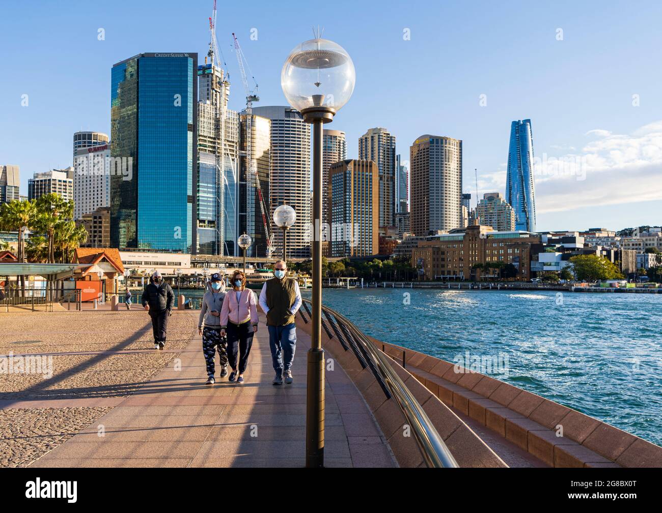 Spaziergänger in Masken trainieren am Circular Quay, Sydney, Australien, während einer Pandemie-Sperre. Blaues Himmel und Skyline im Hintergrund Stockfoto