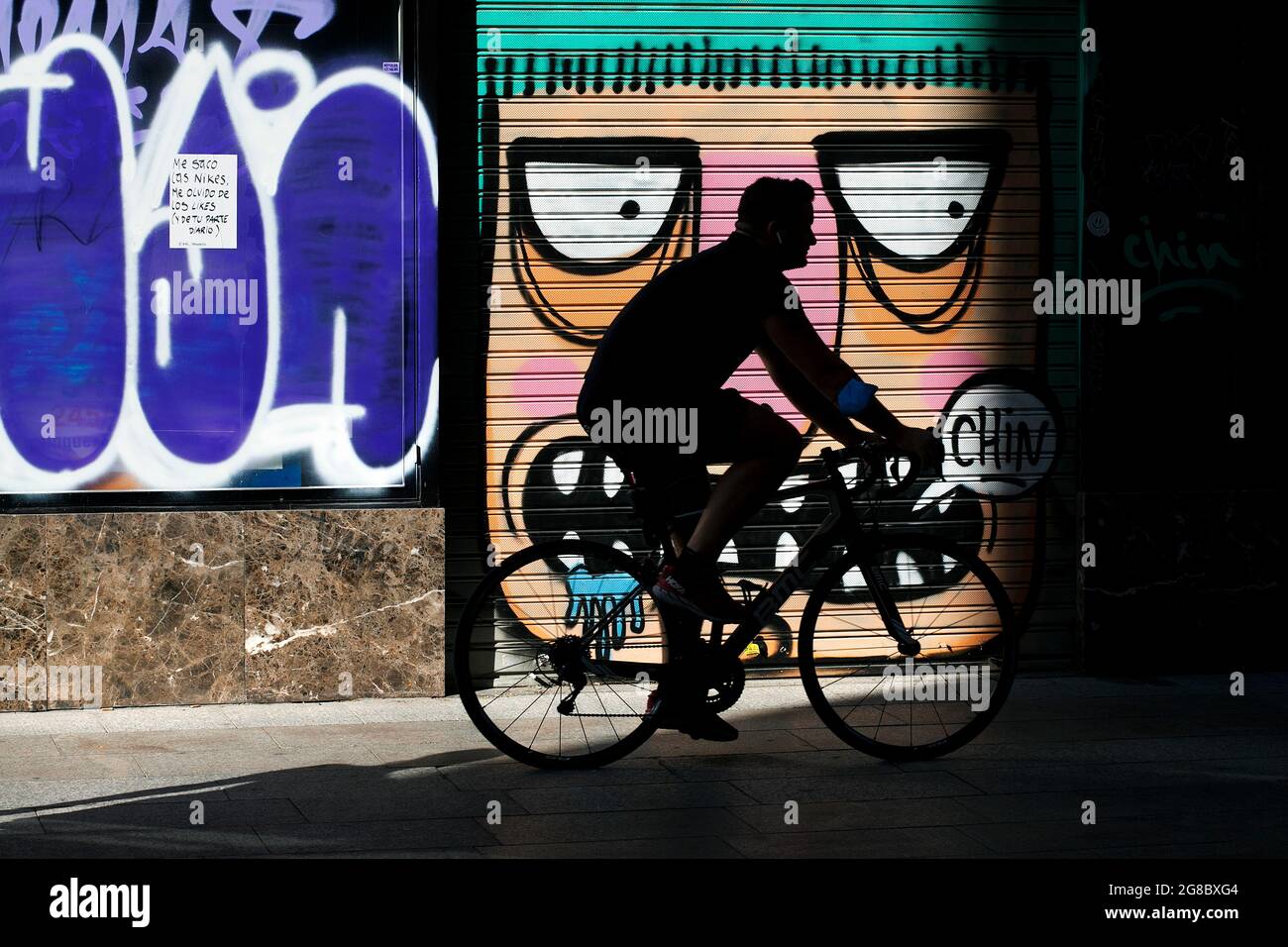 Mann, der auf der Straße an Graffiti vorbeiradelt, Barcelona, Spanien. Stockfoto