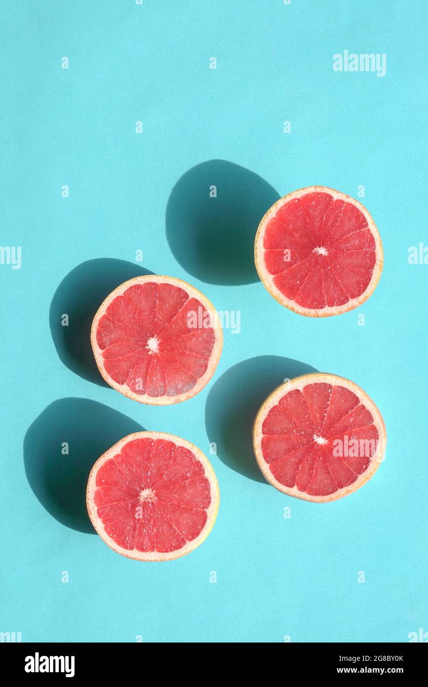 Reife Grapefruithälften auf blauem Hintergrund. Draufsicht auf hartes Sonnenlicht mit Schatten. Stockfoto