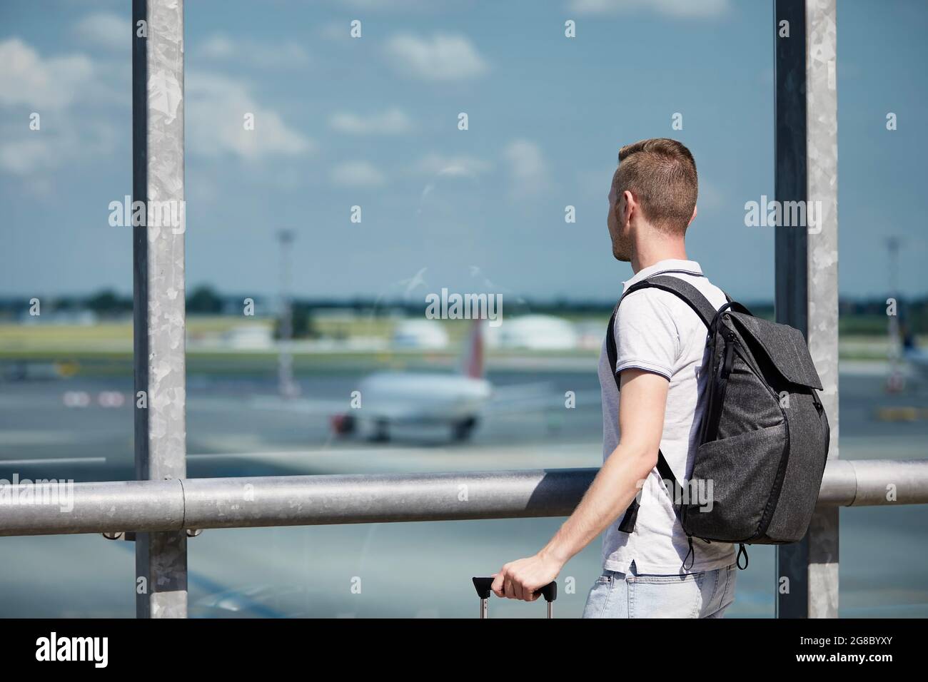 Reisende beobachten Flugzeuge am Flughafen. Rückansicht des Passagiers mit Rucksack, der durch das Fenster des Terminalgebäudes blickt. Stockfoto