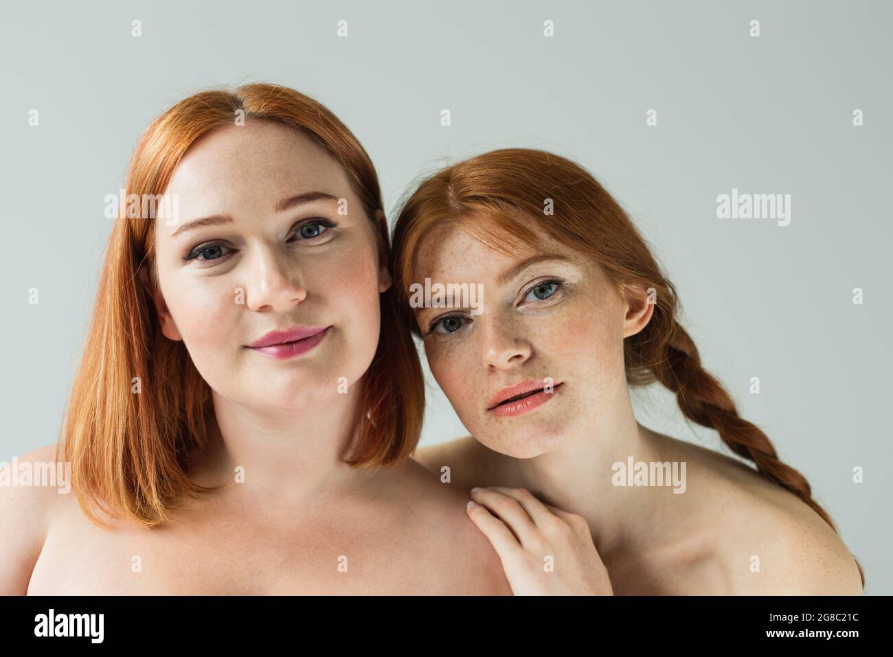 Junge Sommersprossen Frau umarmt plus Größe Freund isoliert auf grau Stockfoto