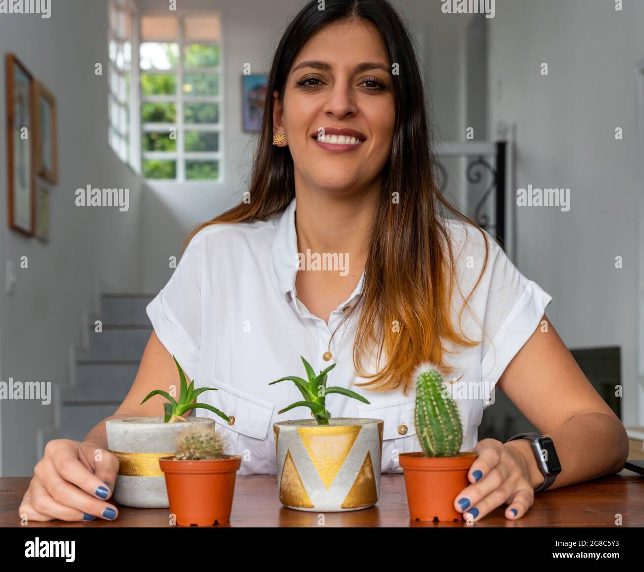 Frau, die zu Hause mit eingetopften Sukkulenten in die Kamera schaut. Stockfoto