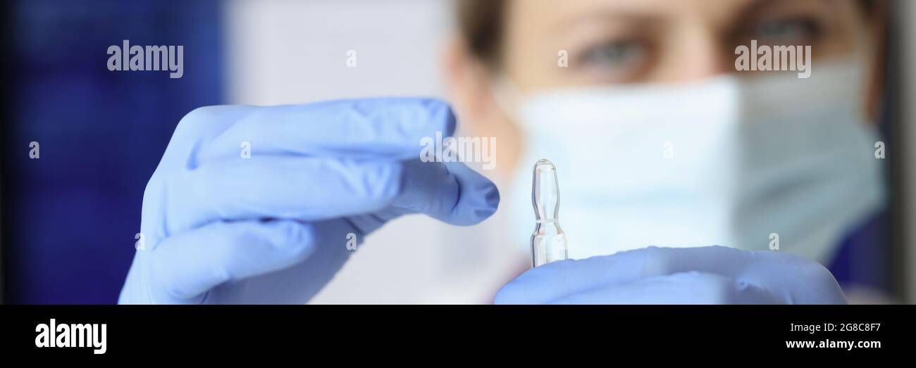 Krankenschwester in Maske und Handschuhe halten Ampulle der Medizin Nahaufnahme Stockfoto