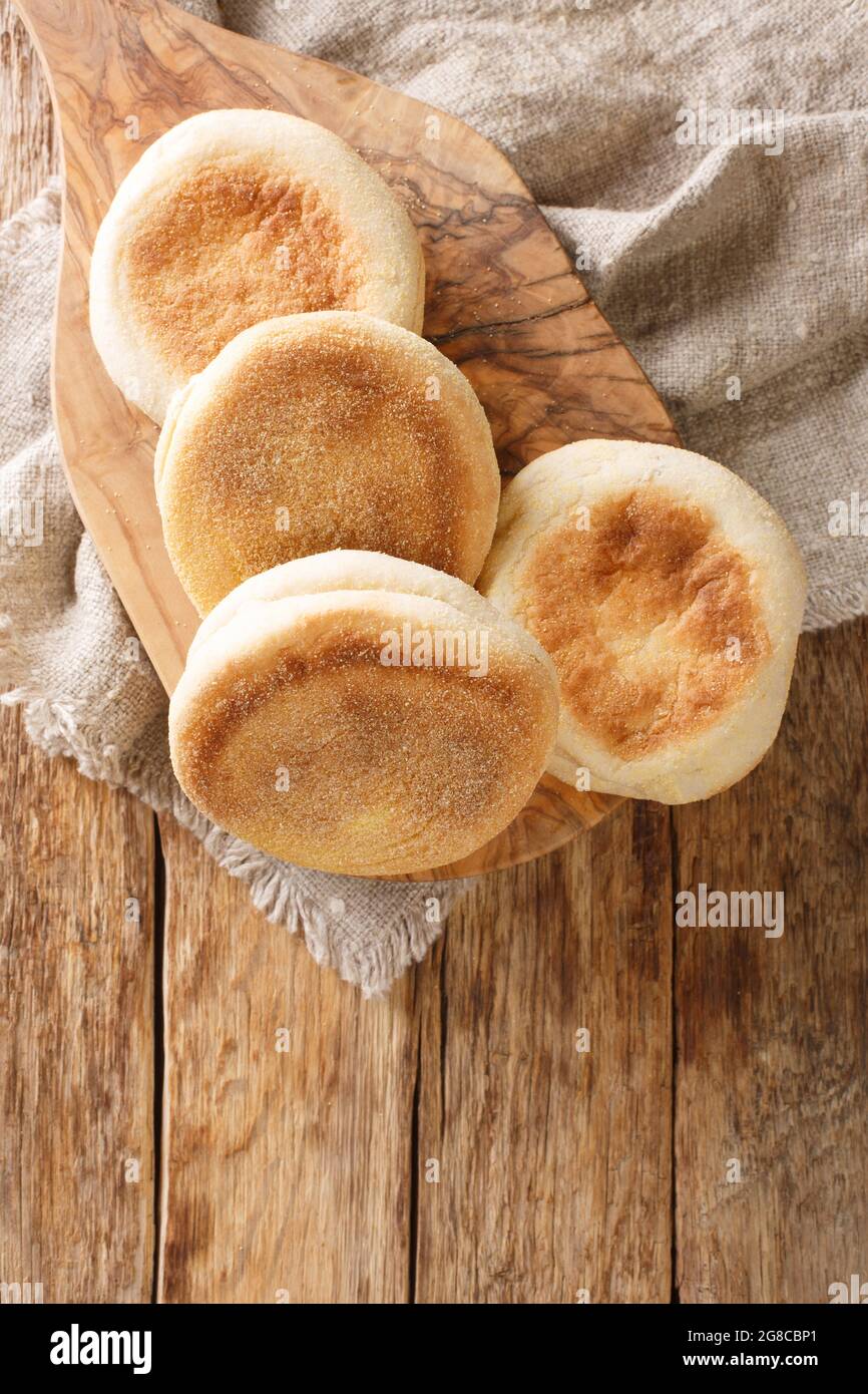 Frisch gebackene englische Muffins aus der Nähe auf einem Brett auf dem Tisch. Vertikale Draufsicht von oben Stockfoto