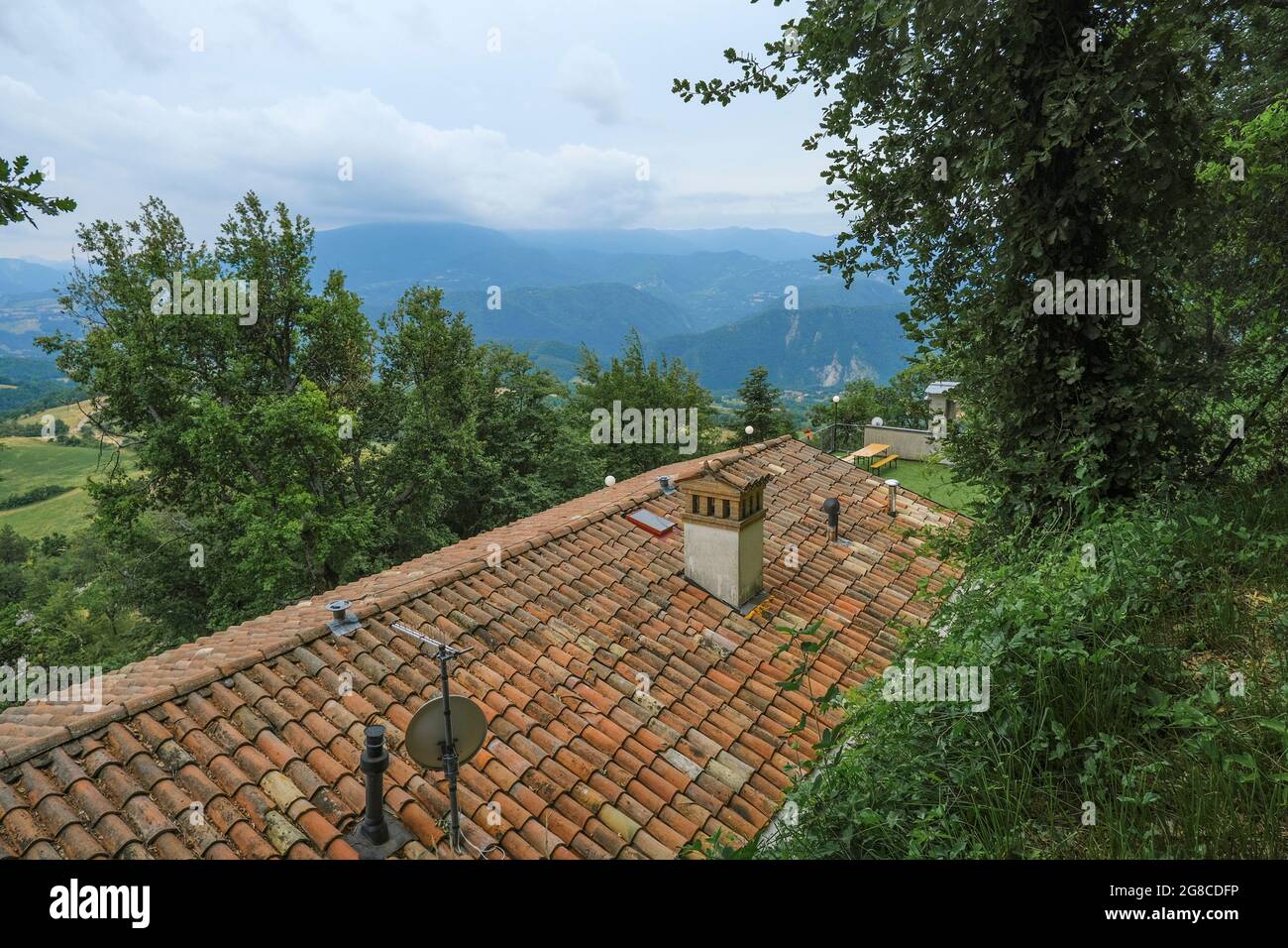 Rotes Ziegeldach des Hauses mit Kamin über die Berge und Bäume Stockfoto