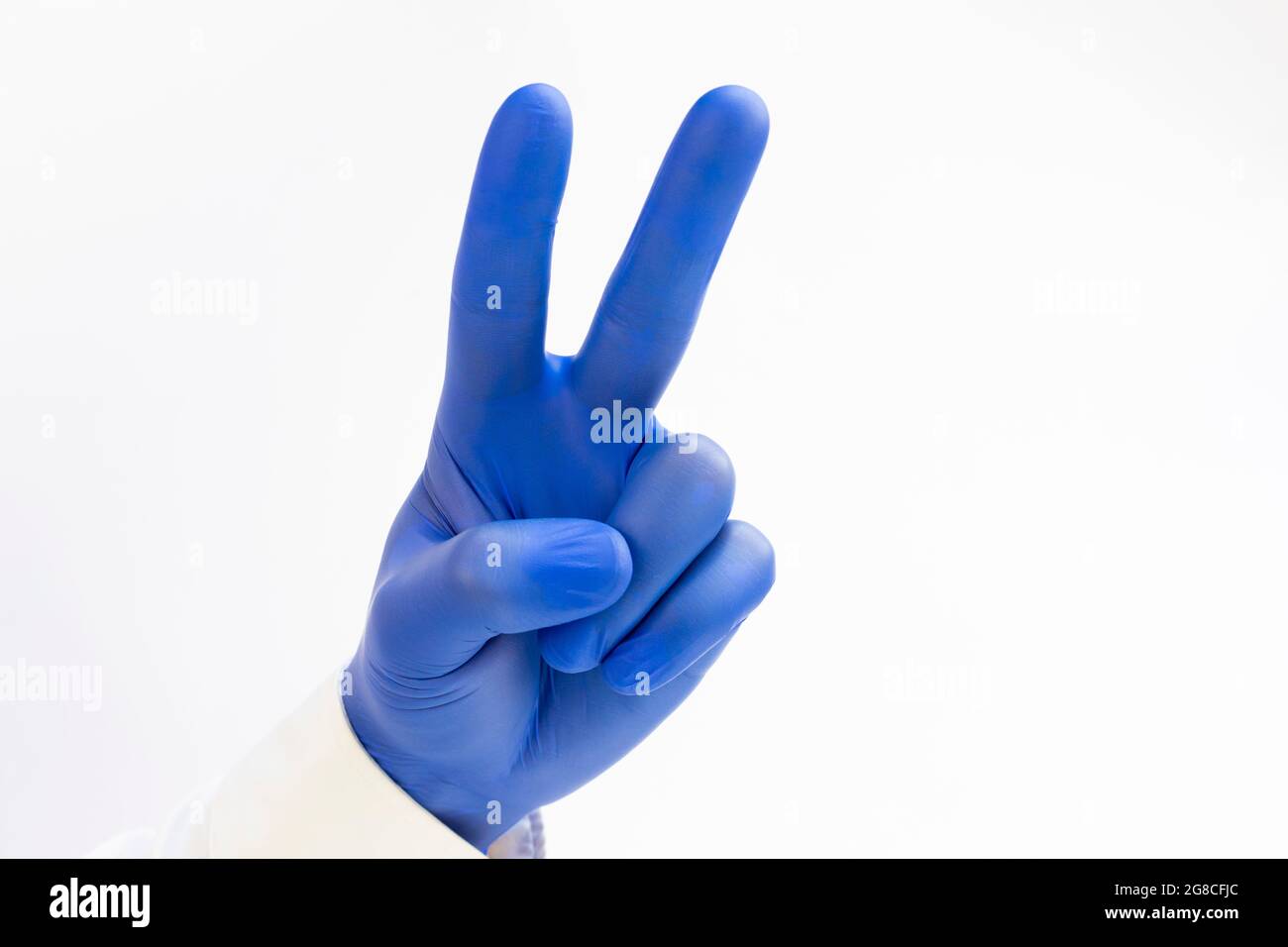 Hand in blauem Latex Handschuh, der zwei Finger auf der Hand hochhebt, zeigt Frieden Stärke Kampf oder Sieg Symbol Stockfoto