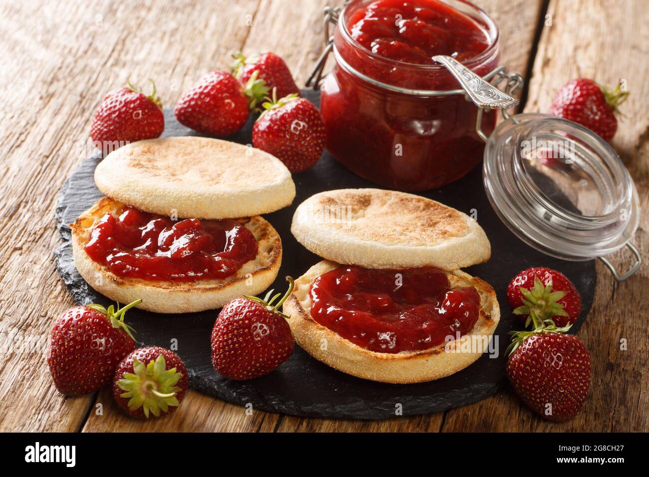 Köstliche klassische englische Muffins mit Erdbeermarmelade aus der Nähe auf einem Schieferbrett auf dem Tisch. Horizontal Stockfoto