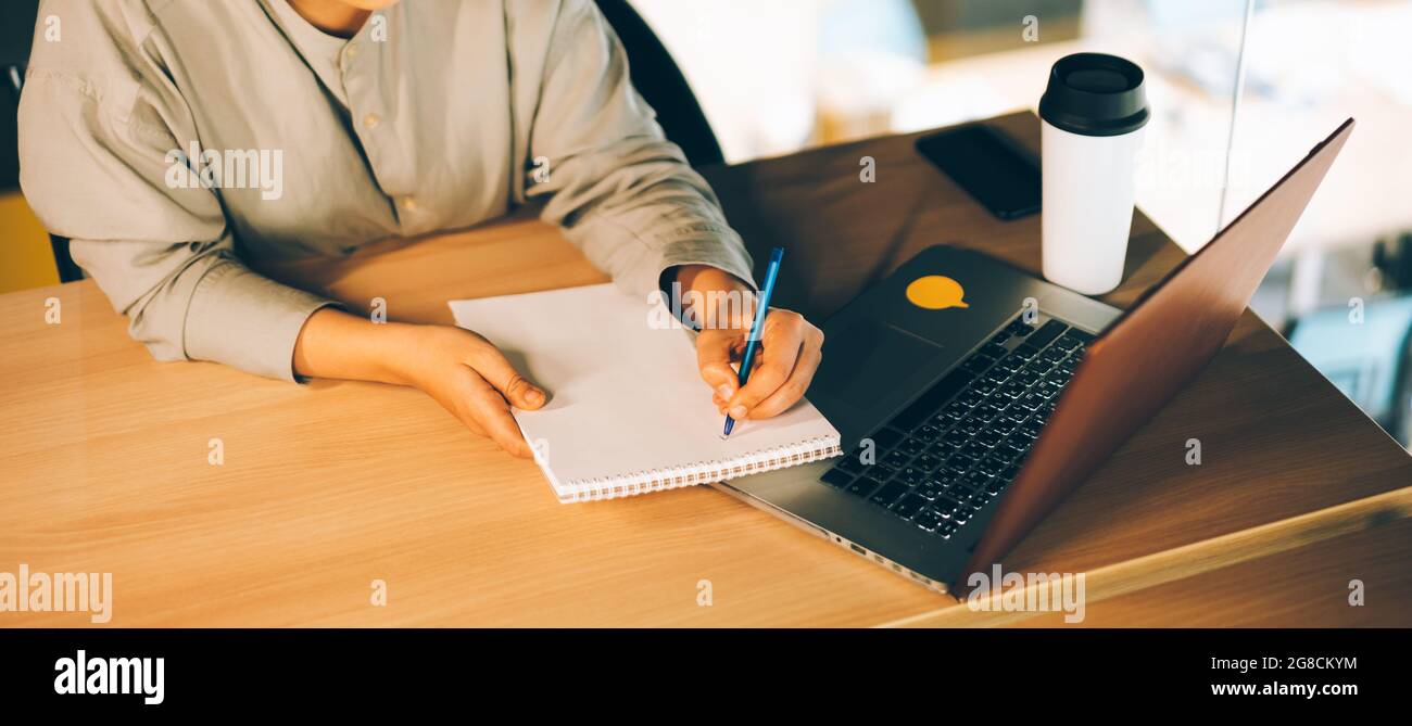 Eine Frau mit Brille studiert online mit ihrem Laptop und schreibt auf einem Notizblock. Einfache Online-Bildung mit Computer- und eLearning-Webinaren Stockfoto