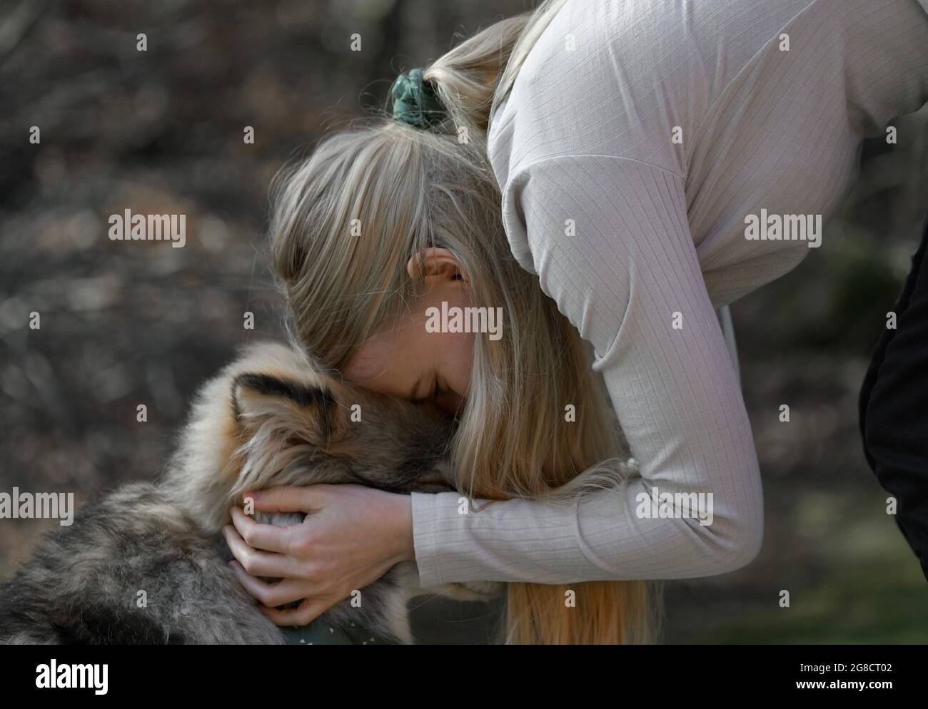 Eine blonde Frau, die mit einem finnischen Lapphund-Hund kuschelt, hat dazu passende Mode-Accessoires Stockfoto