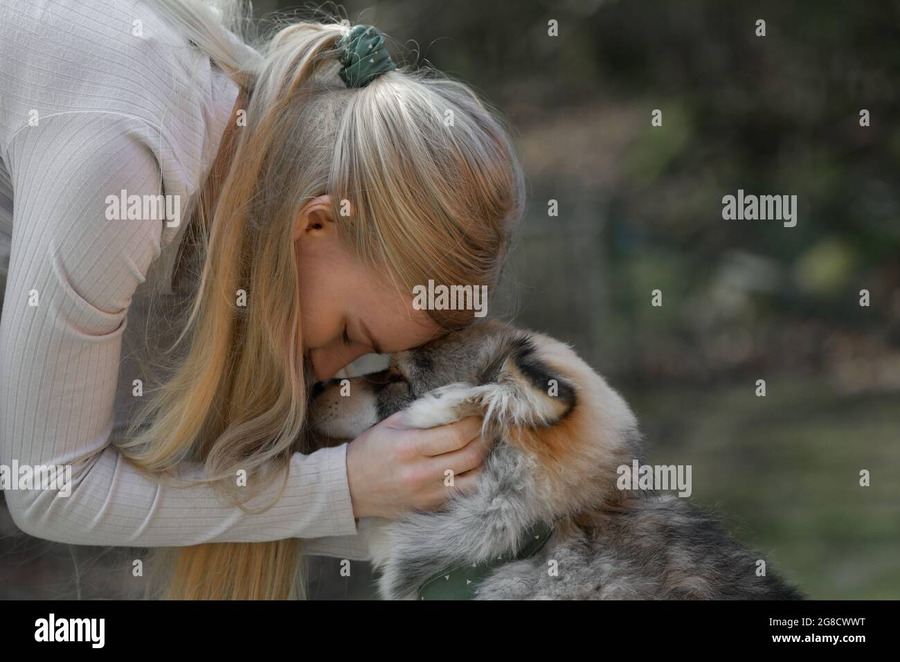 Eine blonde Frau, die mit einem finnischen Lapphund-Hund kuschelt, hat dazu passende Mode-Accessoires Stockfoto