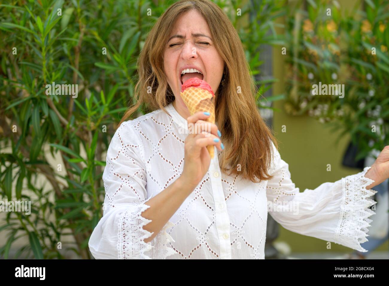 Singende Frau erwartet einen Bissen kalter Beereneis, während sie im Sommer einen Zuckerkonus im Freien gegen Grün bis zum Mund hält Stockfoto