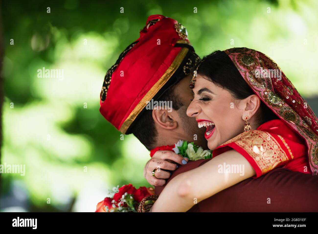 Indischer Mann im Turban umarmt glückliche Braut in traditionellem Kopftuch Stockfoto