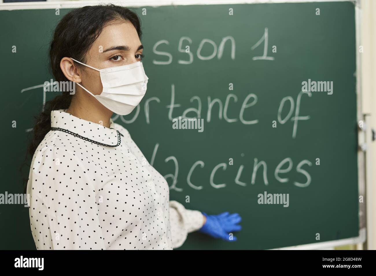 Der Lehrer trägt eine Gesichtsmask und unterrichtet über die Bedeutung von Impfstoffen für die Klasse Stockfoto