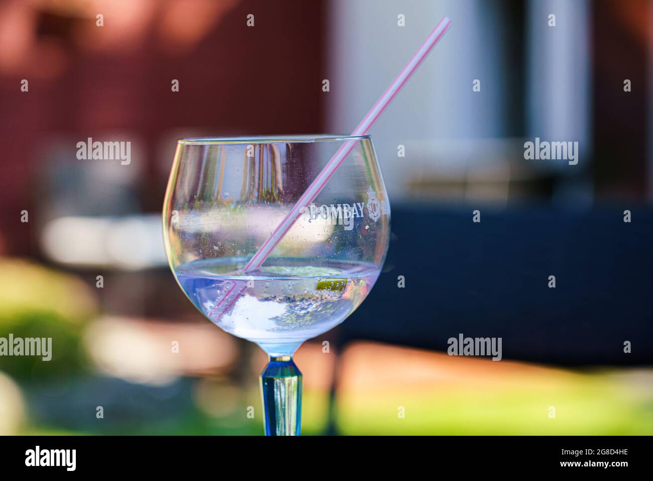 Nahaufnahme eines Bombay Gin and Tonic in einem beschrifteten Glas mit Eis und rosa-weißem Plastikstroh Stockfoto