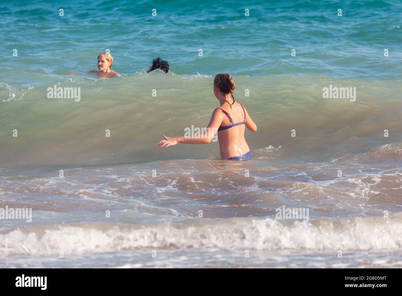 Antalya, Türkei-26. August 2013: Fröhliches, glückliches junges Mädchen, das auf die große Welle im Meer wartet, während zwei andere Personen im Hintergrund schwimmen. Stockfoto