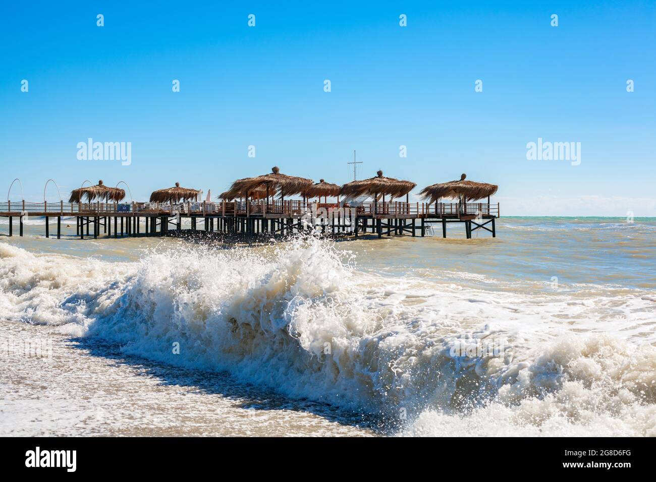 Strandpalmenhütten auf Holzdock in einem welligen Meer. Konzept für das Ende der Sommersaison. Stockfoto