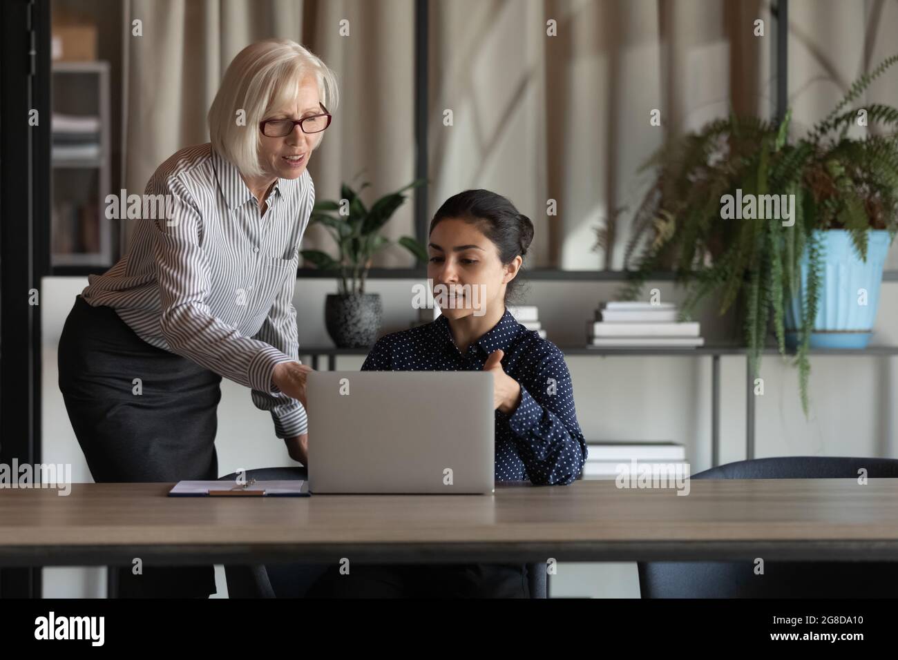 Älterer Mitarbeiter gibt Ratschläge und erklärt dem indischen Mitarbeiter den Arbeitsprozess Stockfoto