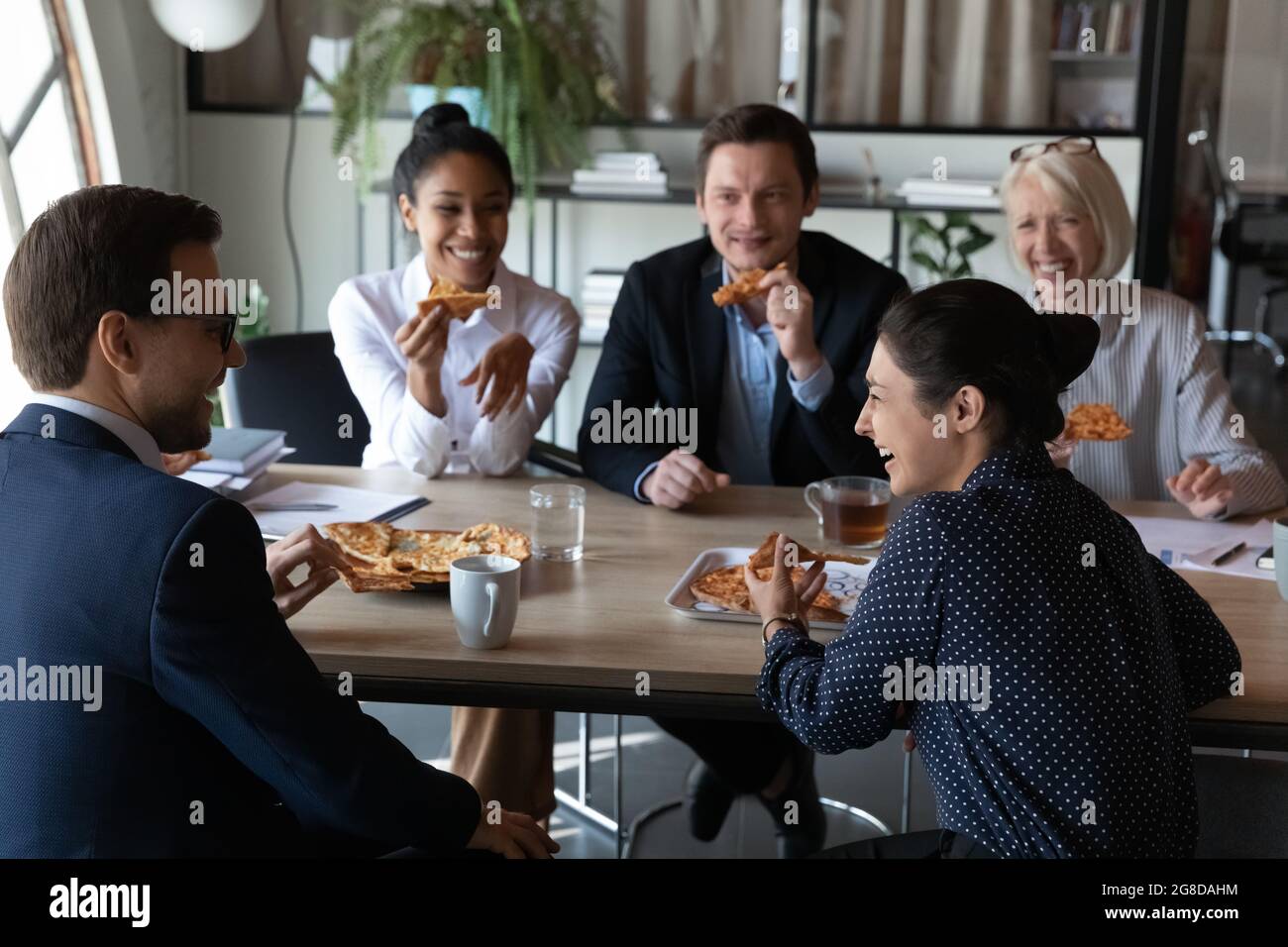 Fröhliche, vielfältige Mitarbeiter genießen eine Pizza-Party am Bürotisch Stockfoto