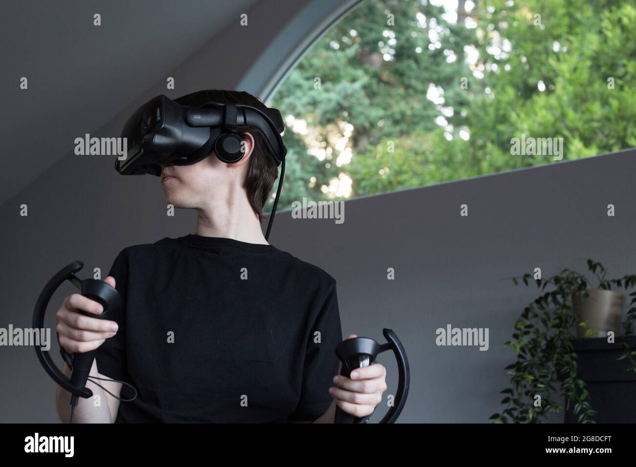 Eine junge nicht-binäre Person, die mit Virtual Reality-Headset und Handtouch-Controllern spielen kann. Stockfoto