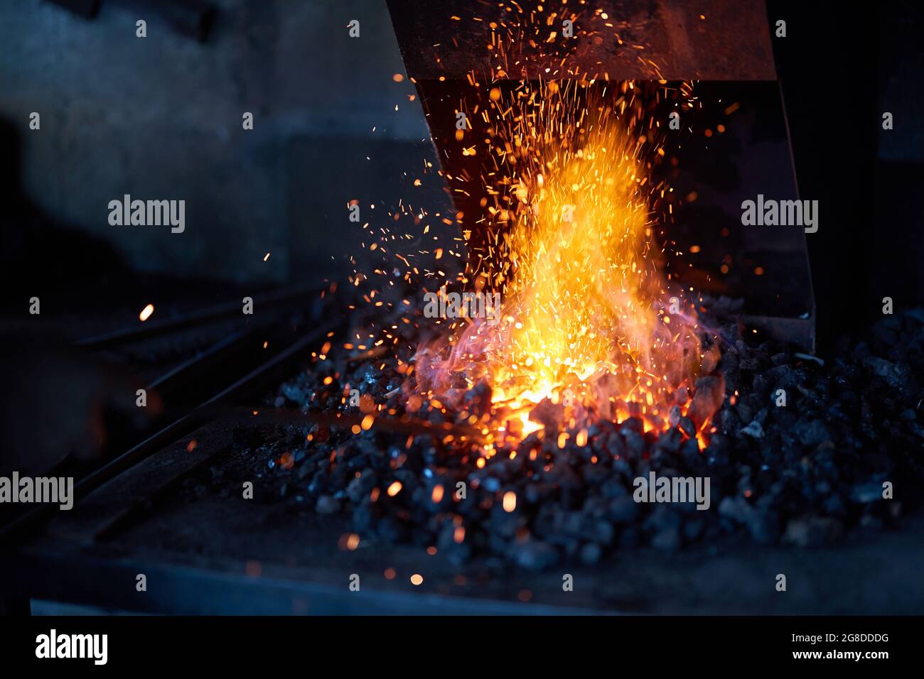 Heißes Rotmetall bei brennendem Feuer zur Vorbereitung auf den Schmiedeprozess in der Werkstatt. Funken fliegen umher. Traditionelle Schmiedekunst. Stockfoto