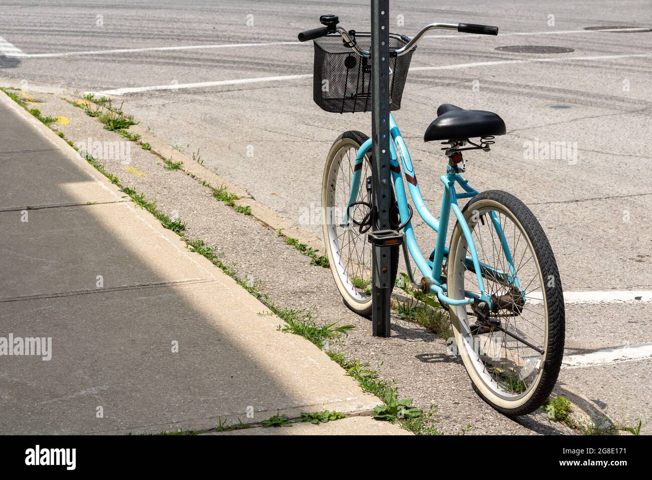 Blaues Cruiser-Fahrrad mit schwarzem Korb, der an einer Verkehrszeichenstange gelehnt und verriegelt ist. Stockfoto