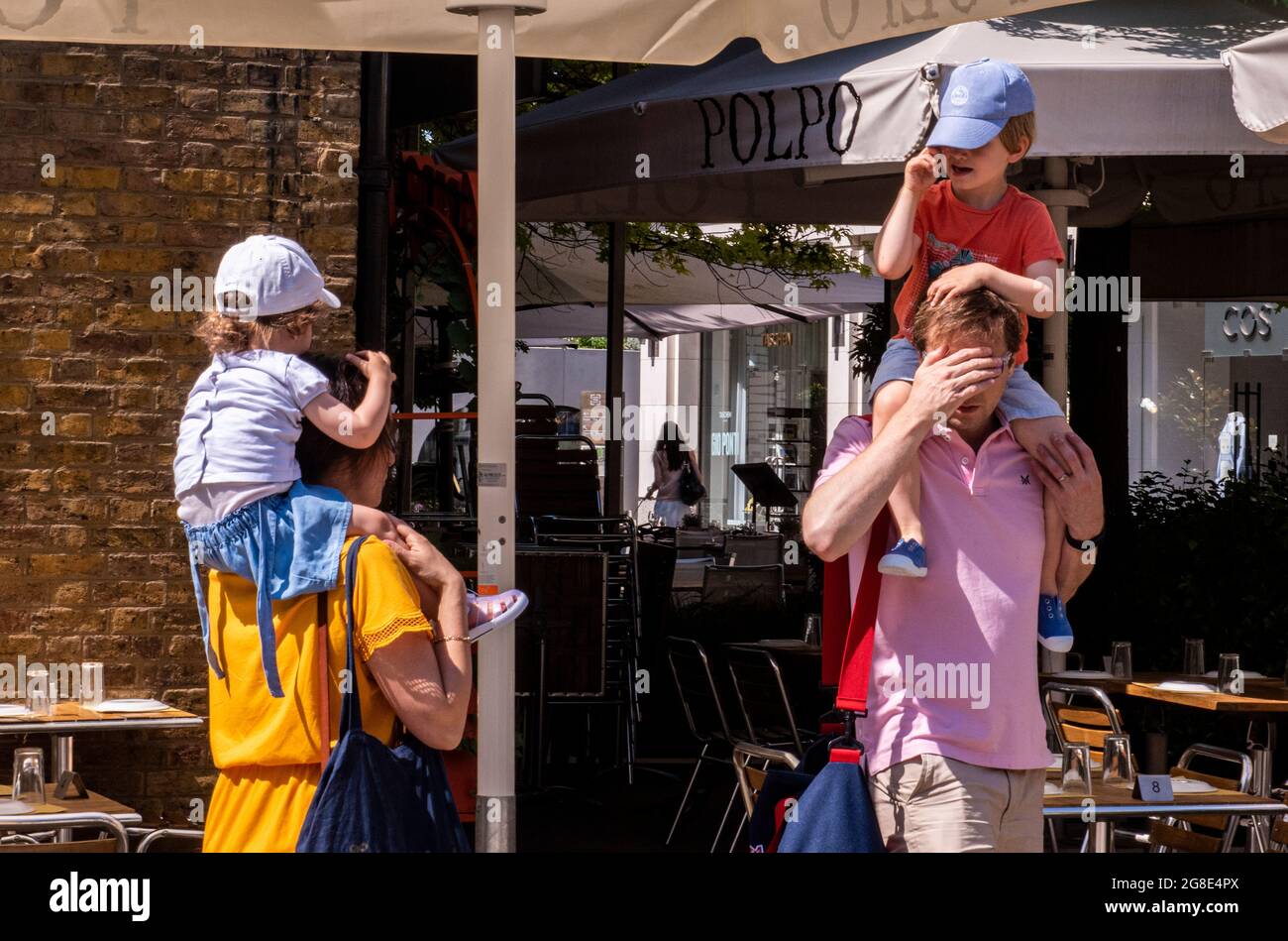 Ein junges Paar, das seine zwei Kleinkinder auf den Schultern trägt, am Sloane Square in London. Stockfoto