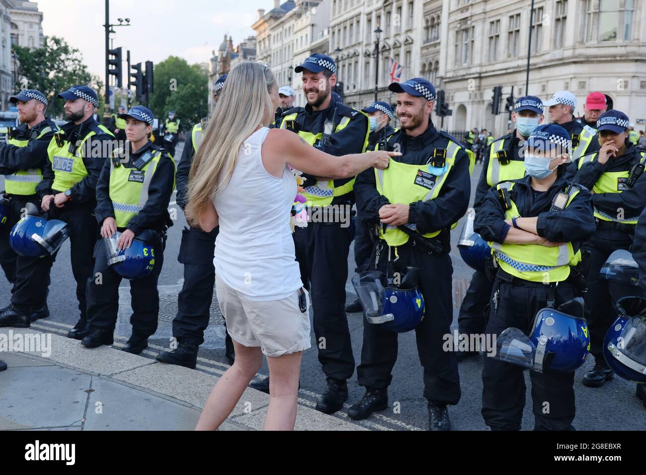Während des „Freedom Day“ tanzt ein Protestler vor einer Polizeilinie - das Lächeln der Polizisten wird sichtbar, wenn Gesichtsmasken optional werden Stockfoto