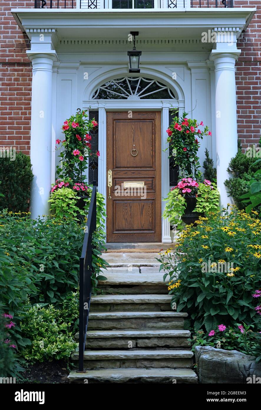 Portico Eingang mit eleganten Holz Maserung Haustür umgeben von bunten Sommerblumen Stockfoto