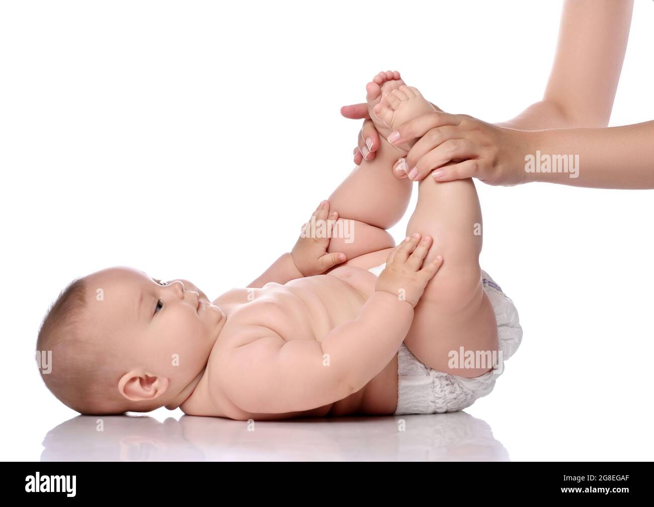 Kleinkind Mädchen Kind in Windel liegt auf ihrem Rücken berühren ihre Knie, während sie Übungen macht, um Muskeln zu stärken Stockfoto