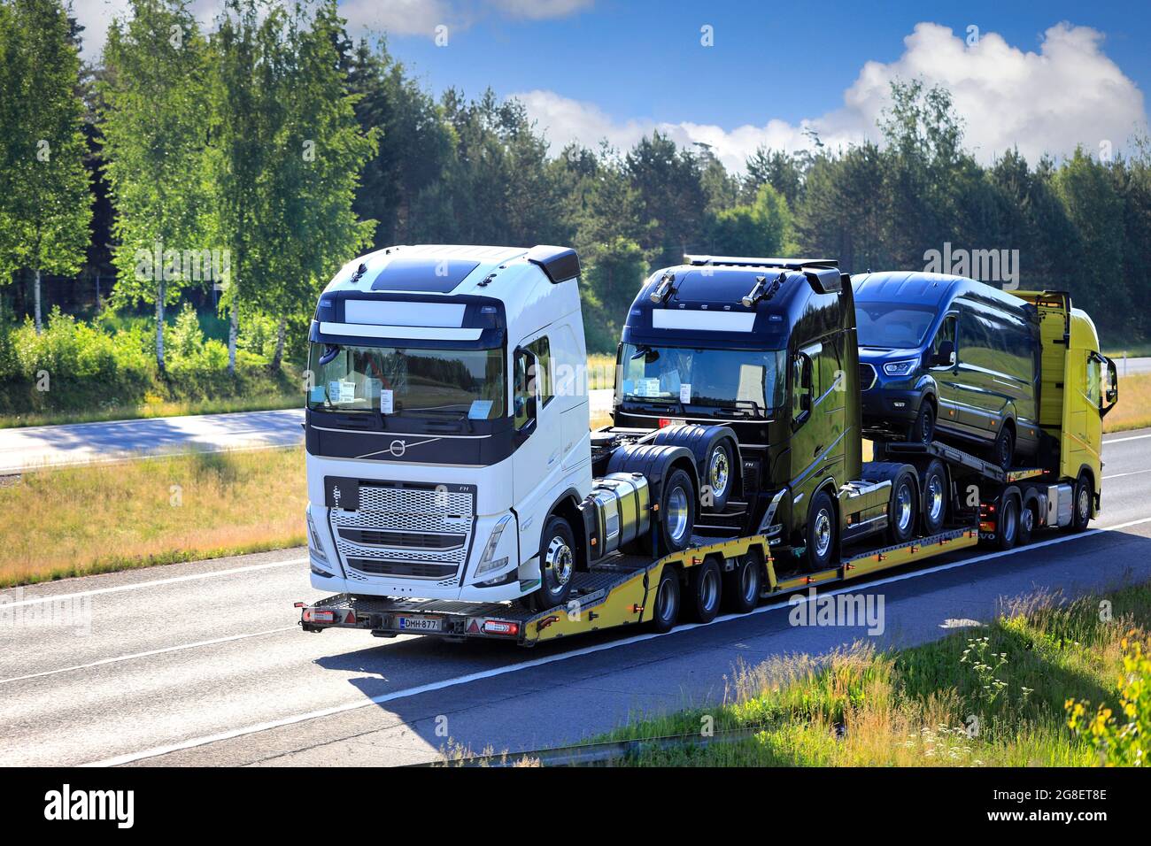 An einem sonnigen Sommermorgen transportiert der LKW zwei neue Volvo Trucks entlang der Autobahn. Salo, Finnland. 11. Juni 2021. Stockfoto