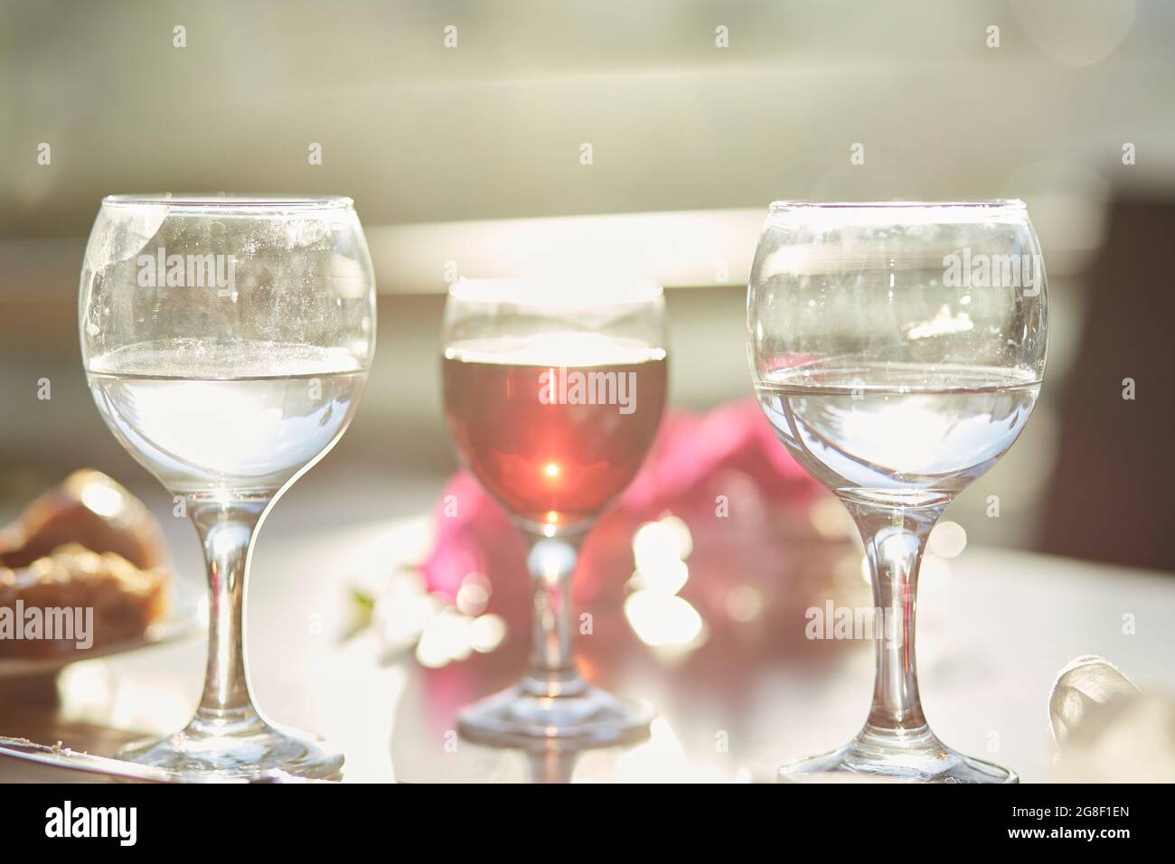 Ein Glas Rotwein und ein Glas Wasser auf dem Tisch. Dekorationen von rosa Bougainvillea Blumen. Speicherplatz kopieren. Stockfoto