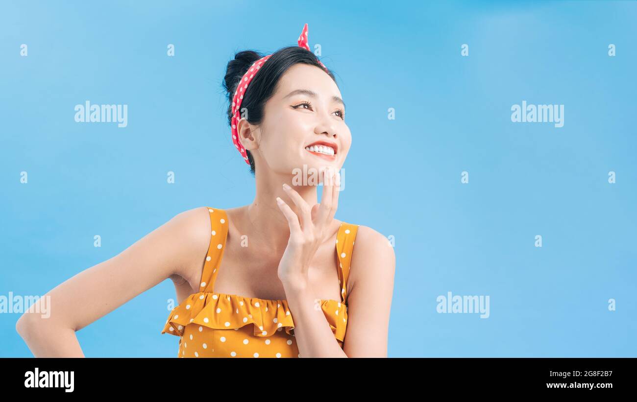 Lächelnd elegante junge Frau in gelbem Kleid im Punktmuster hält die Hand am Kinn und schaut weg Stockfoto