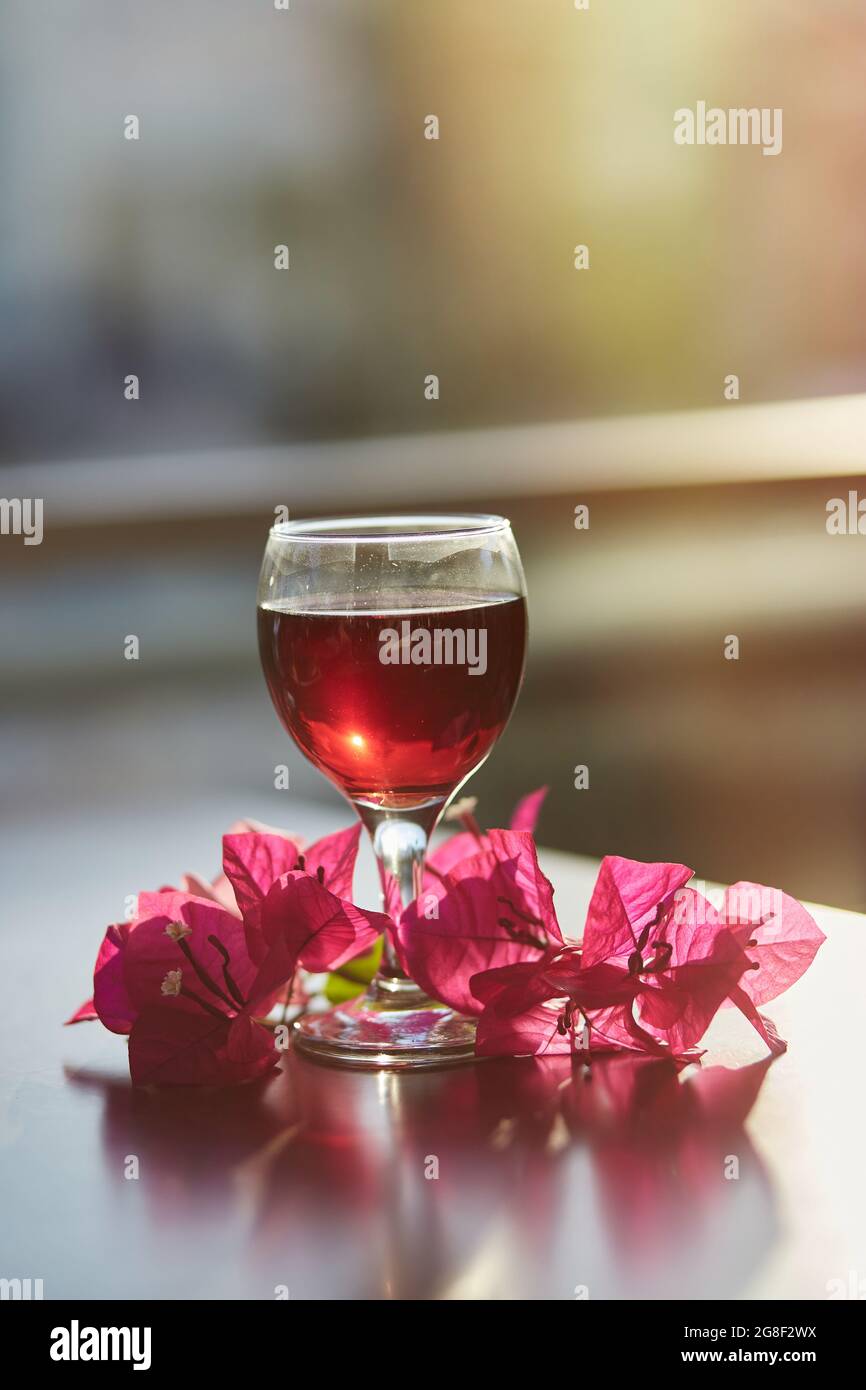 Ein Glas Rotwein auf unscharfem Berghintergrund. Dekorationen von rosa Bougainvillea Blumen mit Sonnenlicht. Blue Hour Fotografie. Romantisches Abendessen Konz Stockfoto
