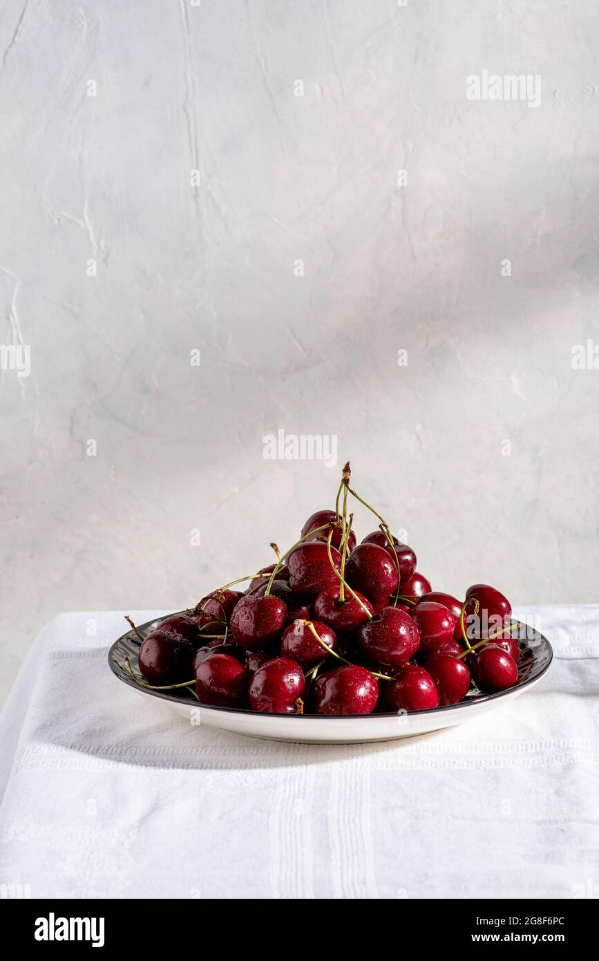 Reife Kirschen auf dem Teller auf dem Tisch mit weißer Tischdecke. Speicherplatz kopieren Stockfoto