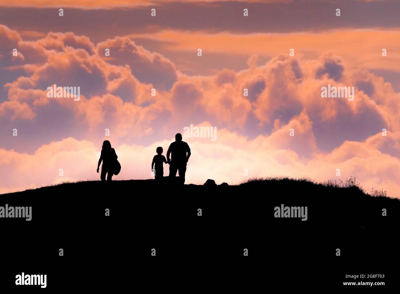 Menschen, die am Ende des Tages in Newquay in Cornwall von einem bunten Himmel auf dem Gipfel des Pentire Point East umragt werden. Stockfoto