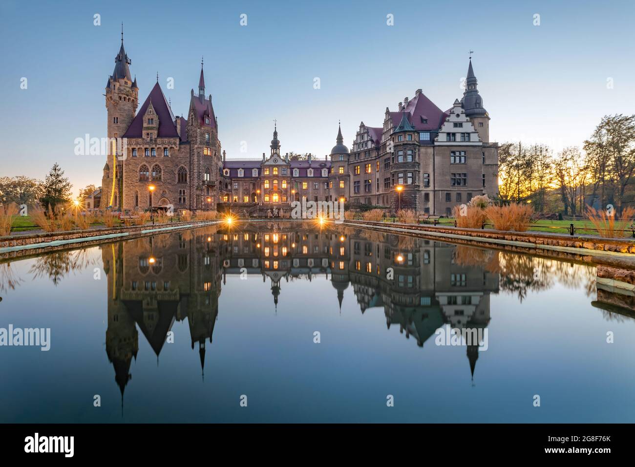 Blick auf das Schloss Moszna (Moszna Zamek), das sich in der Abenddämmerung im Wasser spiegelt, Woiwodschaft Opole, Polen Stockfoto