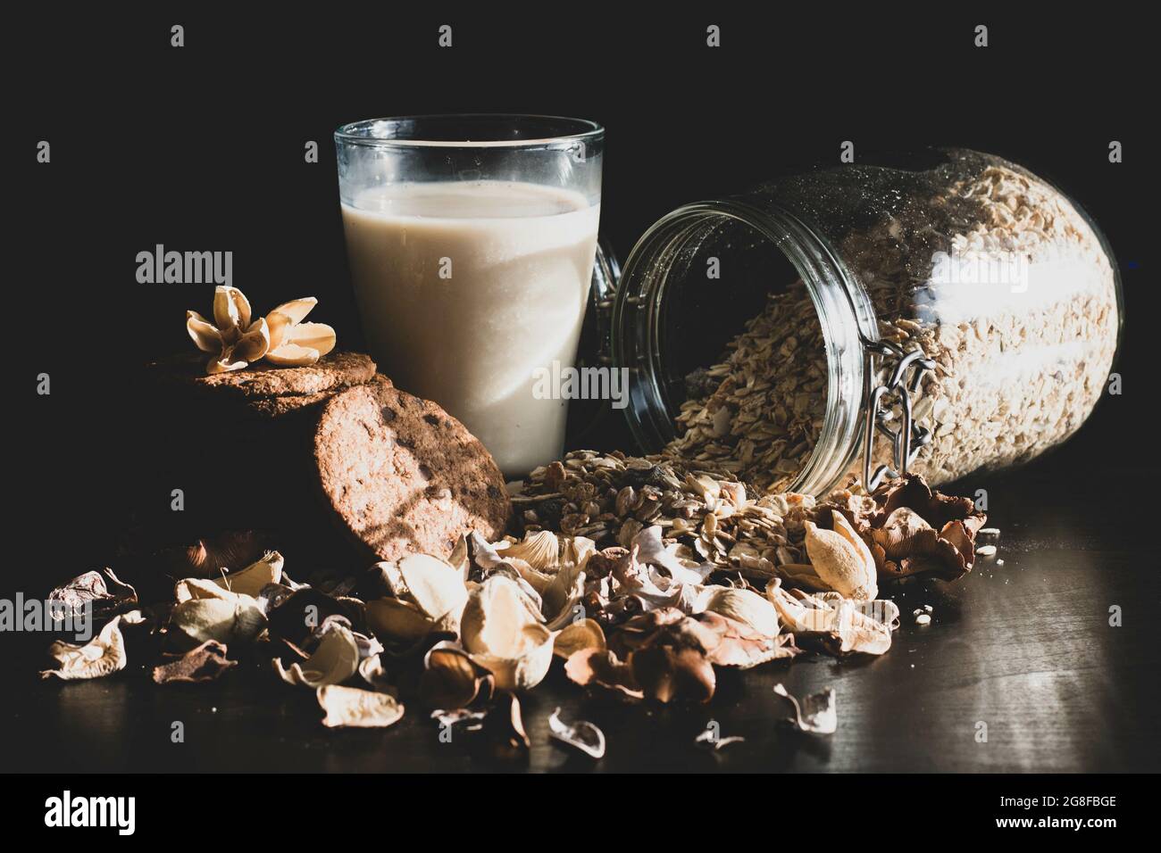 Glas Hafermilch, ein Glas gefüllt mit ganzen Haferkörnern und Keksen auf schwarzem Hintergrund Stockfoto