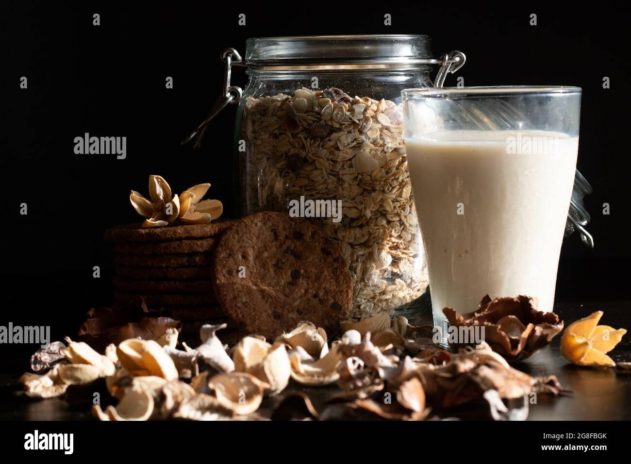 Glas Hafermilch, ein Glas gefüllt mit ganzen Haferkörnern und Keksen auf schwarzem Hintergrund Stockfoto
