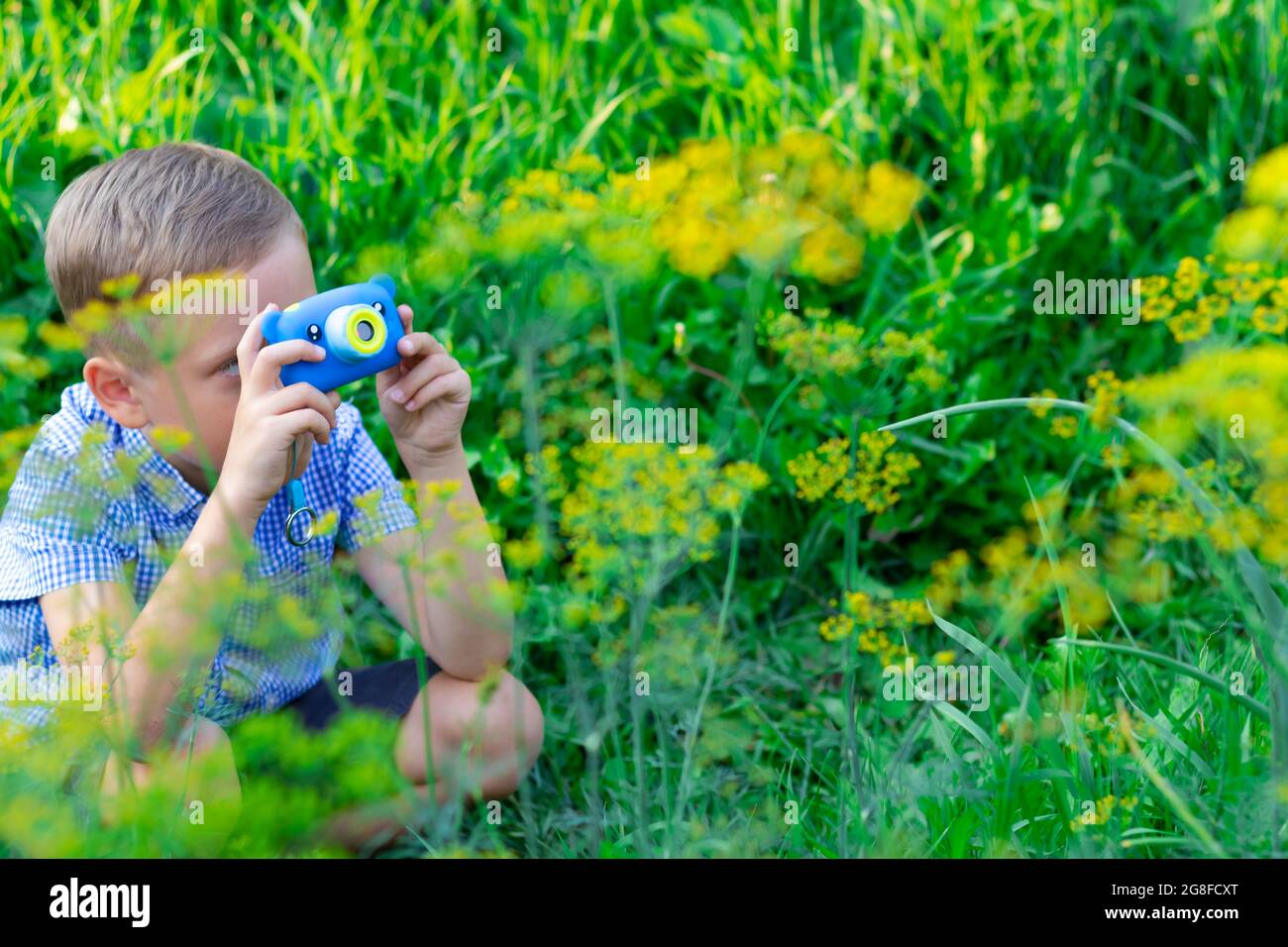 Ein süßer Vorschuljunge mit einer hübschen Frisur in einem blauen Hemd fotografiert an einem heißen Sommertag grüne Pflanzen. Selektiver Fokus. Hochformat Stockfoto