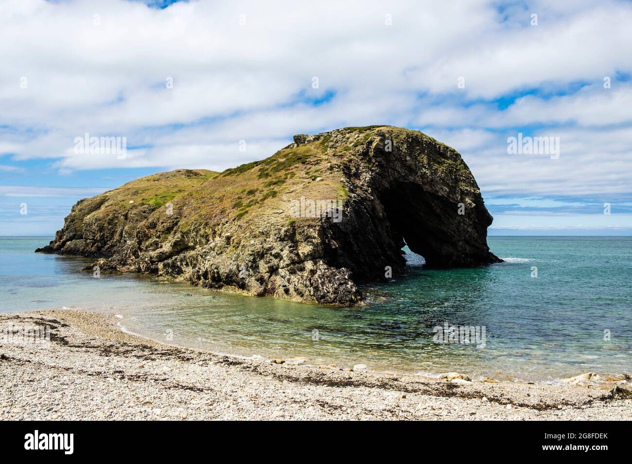 Kiesstrand und Ynys y Fydlyn Felseninsel mit Bogen bei Flut in der Nähe von Carmel Head an der Küste. Isle of Anglesey, Nordwales, Großbritannien Stockfoto