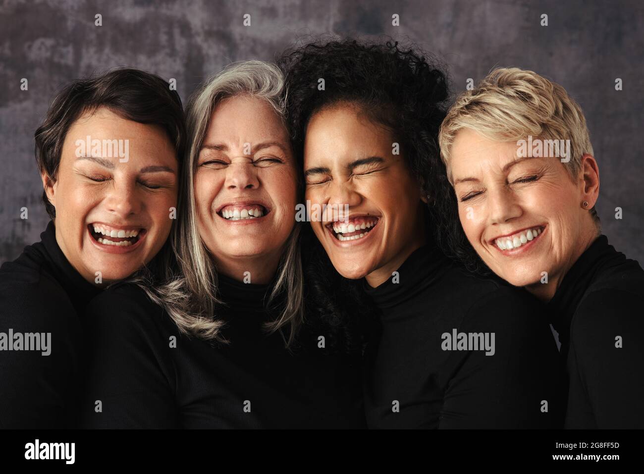 Nahaufnahme verschiedener Frauen, die fröhlich in einem Studio lächeln. Vier selbstbewusste Frauen unterschiedlichen Alters umarmen ihre natürlichen und alternden Körper während der Standzeit Stockfoto